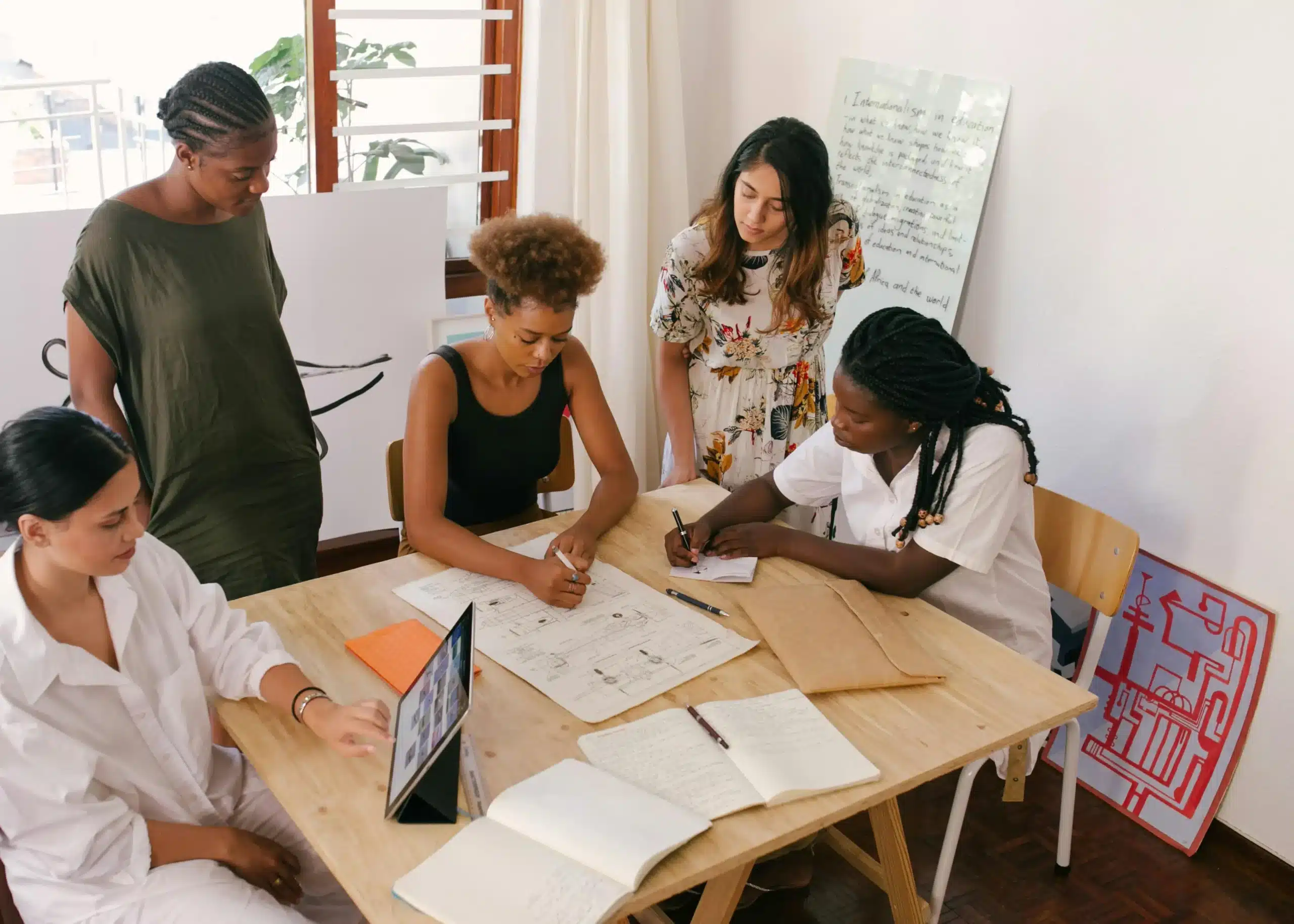 Eine Gruppe von Frauen sitzt und steht um einen Tisch herum und arbeitet. (Foto: RF._.studio/Pexels)