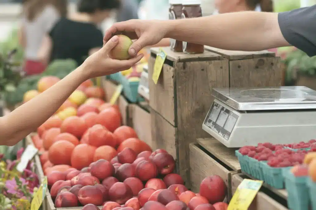 Ein Händler an einem Obststand gibt einer Kundin eine Frucht. (Foto: Pexels)