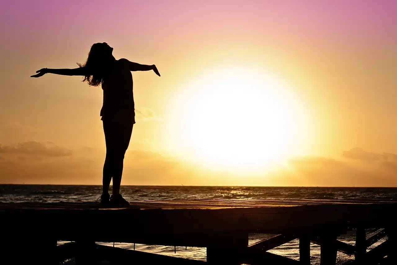 Eine Frau breitet vor der Sonne die Arme aus. (Foto: Jill Wellington/ Pixabay)