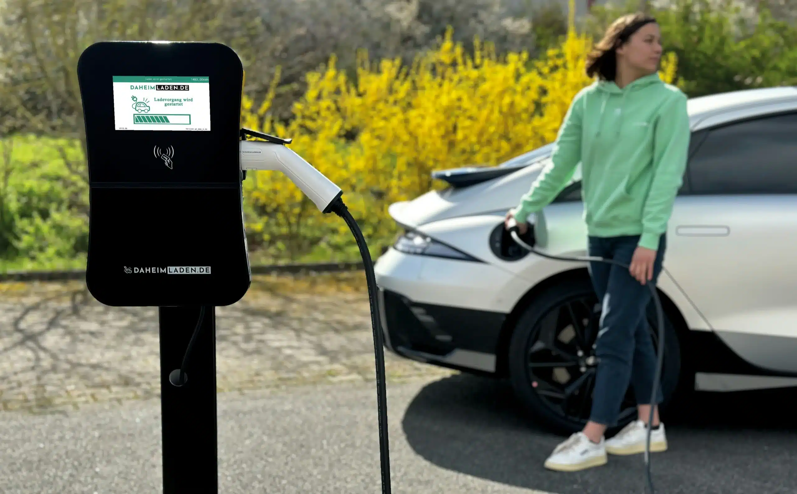 Eine Wallbox steht vor einem weißen Auto und einer Frau. (Foto: Stephan Schwebe/Unsplash)