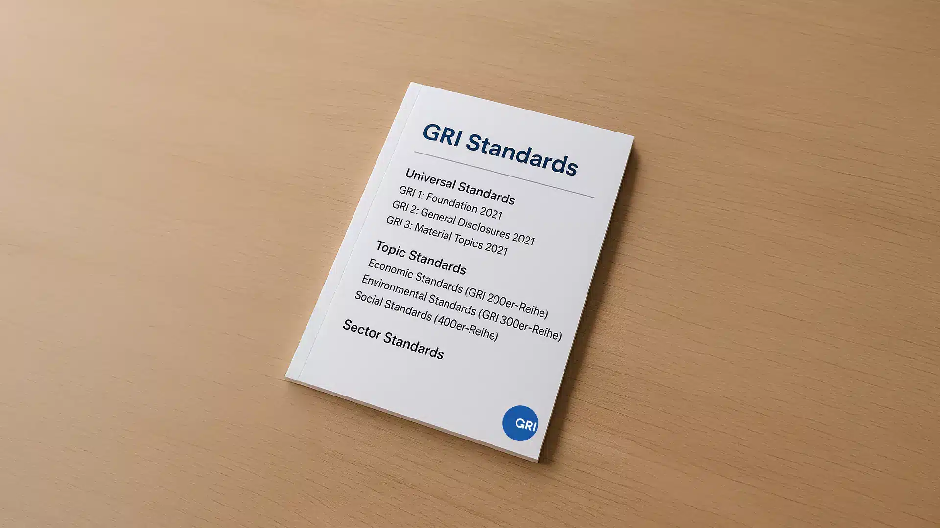 Auf einer hellen Holzoberfläche liegt eine Broschüre mit dem Titel „GRI-Standards“ der Global Reporting Initiative. Auf dem Cover sind in blauer und schwarzer Schrift universelle Standards, themenbezogene Standards (wirtschaftlich, ökologisch, sozial) und sektorbezogene Standards aufgeführt.