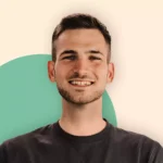 Ein junger Mann mit kurzen braunen Haaren und heller Gesichtsbehaarung lächelt in die Kamera. Er trägt ein dunkles T-Shirt mit der Aufschrift "EEAktuell" - eine Anspielung auf Erneuerbare Energien. Der Hintergrund ist hell mit einem grünen Halbkreis hinter ihm.