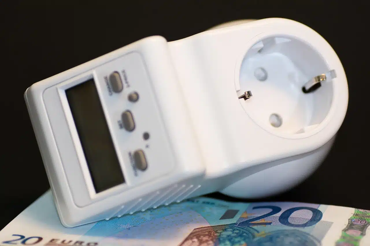 Ein digitaler Stromzähler mit Tasten und einem Bildschirm ruht auf einer 20-Euro-Banknote vor schwarzem Hintergrund.
