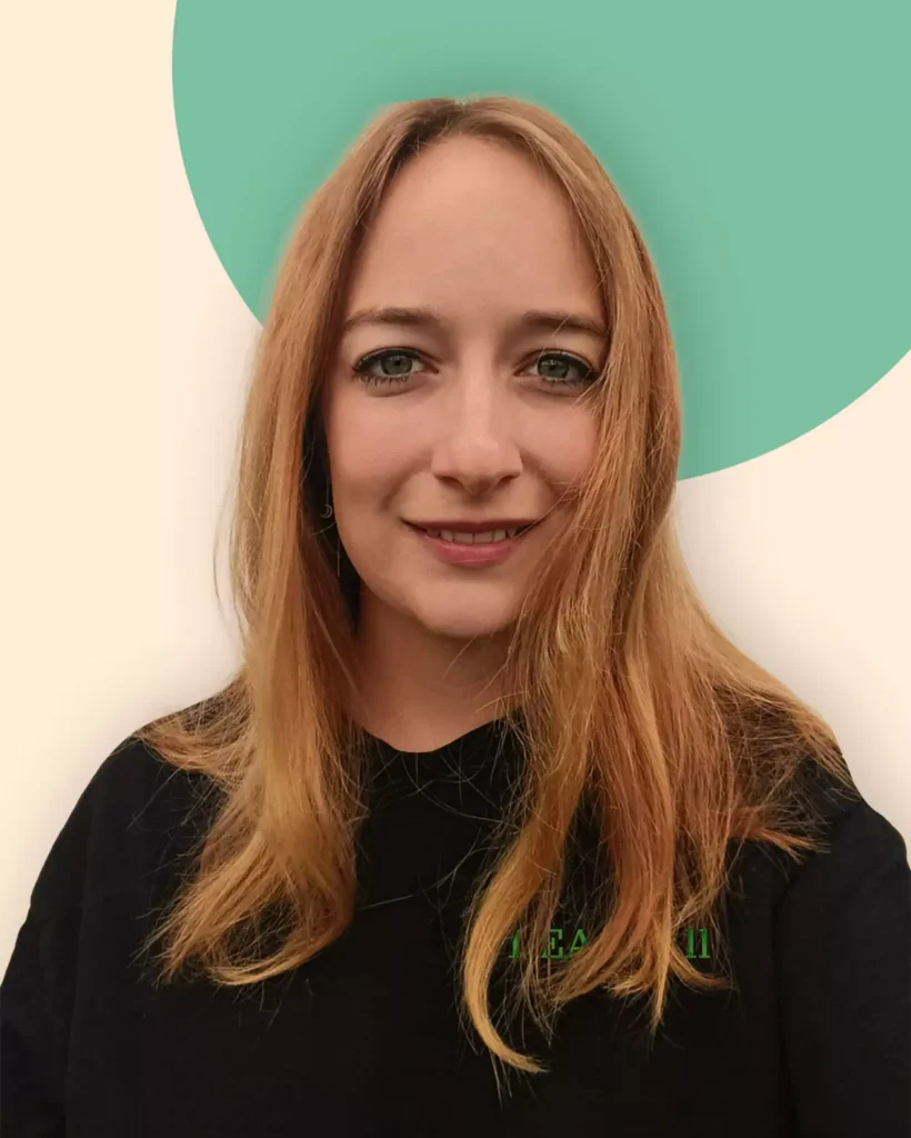 Eine Frau mit langen, hellbraunen Haaren und einem schwarzen Oberteil lächelt in die Kamera. Der Hintergrund ist beige mit einem großen grünen Kreis hinter ihrem Kopf, der ihr Engagement für Erneuerbare Energien symbolisiert.