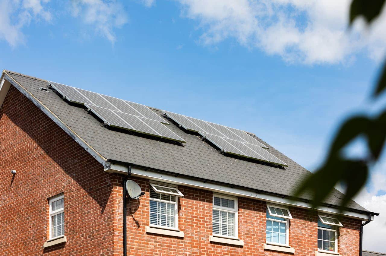 Ein Backsteinhaus mit drei Solarpaneelen auf dem dunkelgrauen Dach unter einem teilweise bewölkten blauen Himmel.