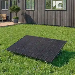 Ein einzelnes schwarzes Solarmodul ist auf einer Rasenfläche vor einem modernen dunklen Holzhaus mit großen Fenstern und einem kleinen Innenhof mit einer Bank und Topfpflanzen installiert.