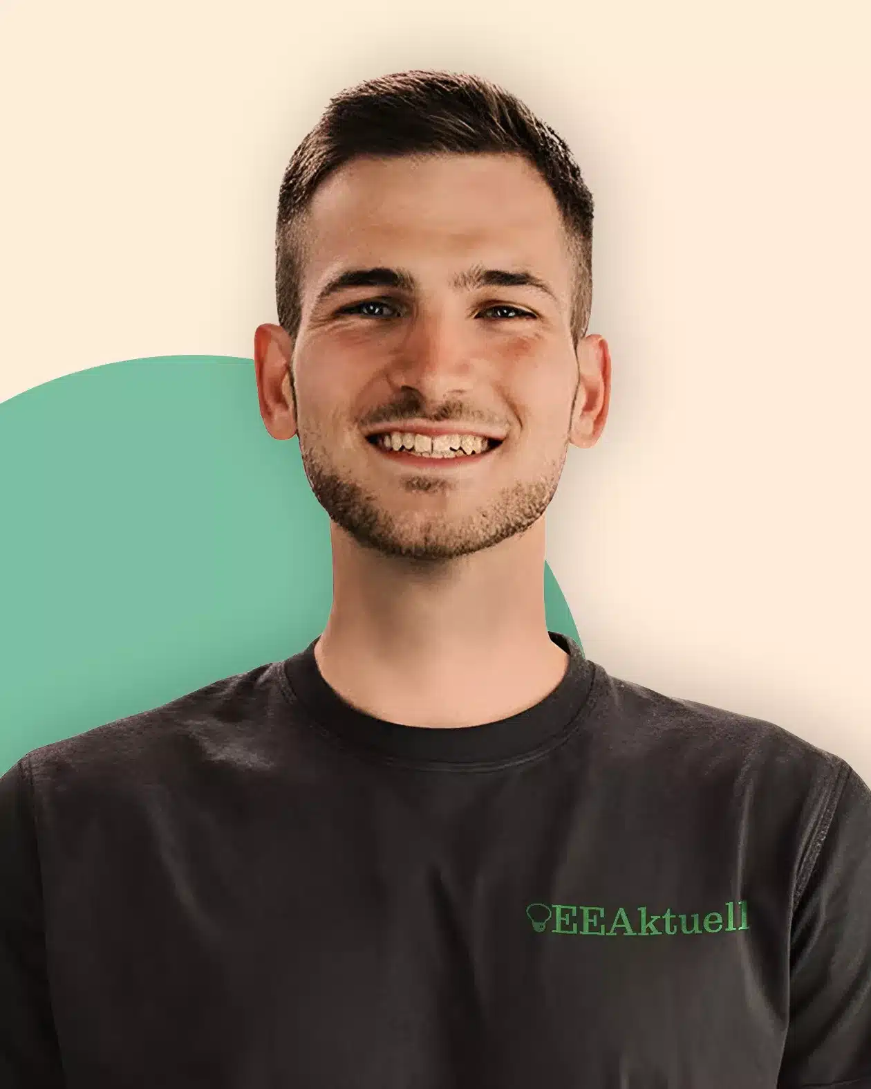 Ein junger Mann mit kurzen braunen Haaren und gestutztem Bart lächelt, er trägt ein dunkles T-Shirt mit dem Aufdruck EEAktuell in Grün und steht vor einem beigefarbenen Hintergrund mit einem grünen Kreisakzent, der Erneuerbare Energien symbolisiert.