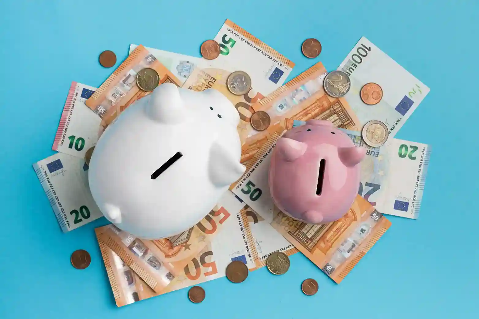 Zwei Sparschweine, ein weißes und ein rosafarbenes, sitzen auf verschiedenen Euro-Banknoten und verstreuten Euro-Münzen vor einem blauen Hintergrund und symbolisieren eine clevere Tagesgeld-Alternative zum Sparen.