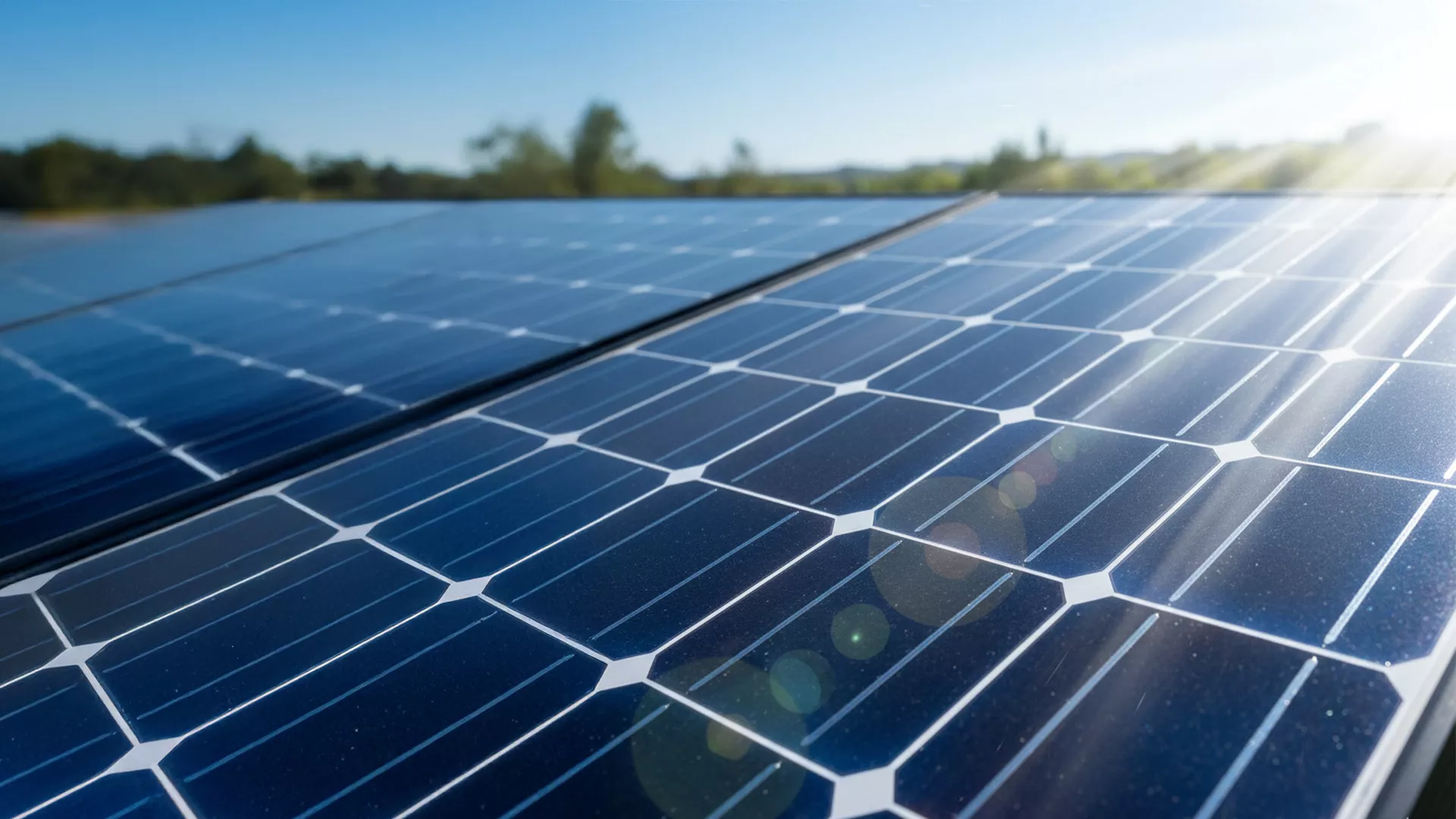 Nahaufnahme von glänzenden blauen Solarmodulen im hellen Sonnenlicht, mit Bäumen und blauem Himmel im unscharfen Hintergrund. Die Sonnenstrahlen erzeugen Linsenreflexe auf der Oberfläche der Paneele.