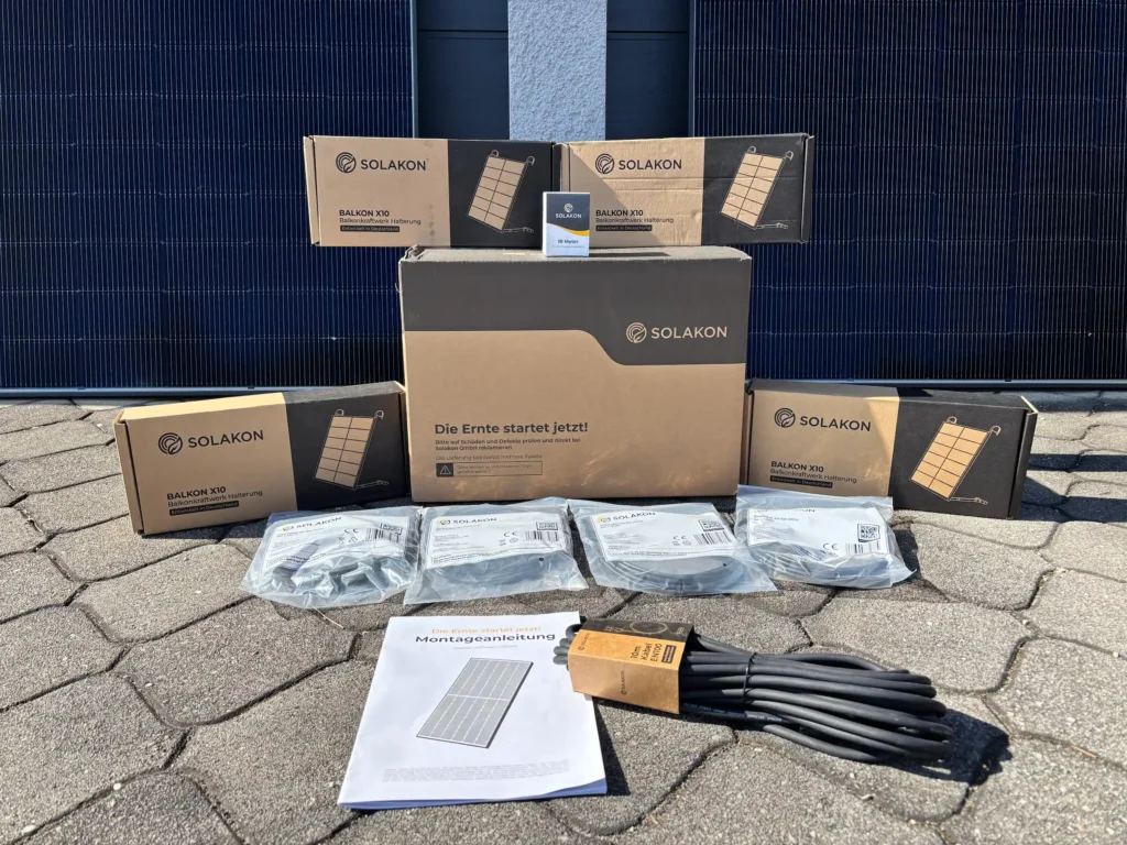 SOLAKON BALKON X10 Solarmodul-Montagesatz mit Kabeln und Anleitung auf einer Terrasse ausgelegt, um die einfache Installation und zuverlässige Qualität zu demonstrieren, inspiriert durch positive Solakon Erfahrungen, mit Solarmodulen im Hintergrund.