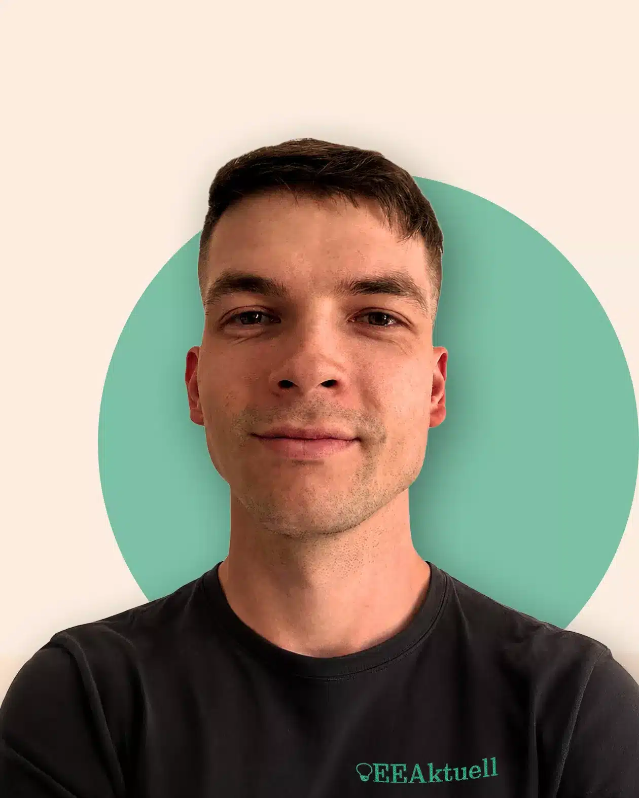 Ein junger Mann mit kurzen braunen Haaren und einem leichten Lächeln trägt ein dunkles „EEAktuell“-T-Shirt und steht vor einem hellen Hintergrund, der durch einen grünen Kreis hinter ihm hervorgehoben wird.