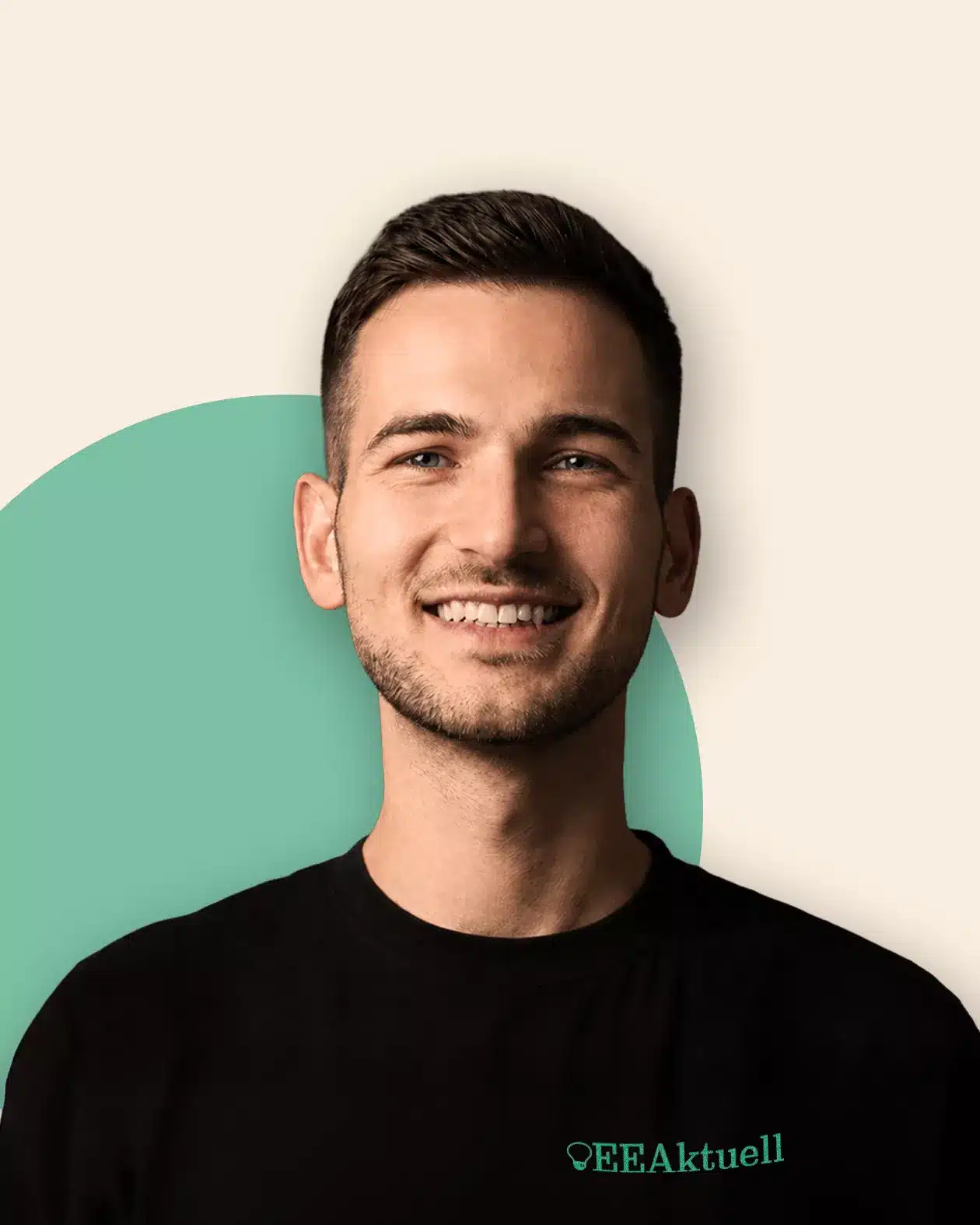 Ein junger Mann mit kurzen braunen Haaren und einem gepflegten Bart lächelt in die Kamera. Er trägt ein schwarzes „EEAktuell“-T-Shirt mit grünem Logo. Der Hintergrund ist beige und wird durch einen blaugrünen Halbkreis akzentuiert.