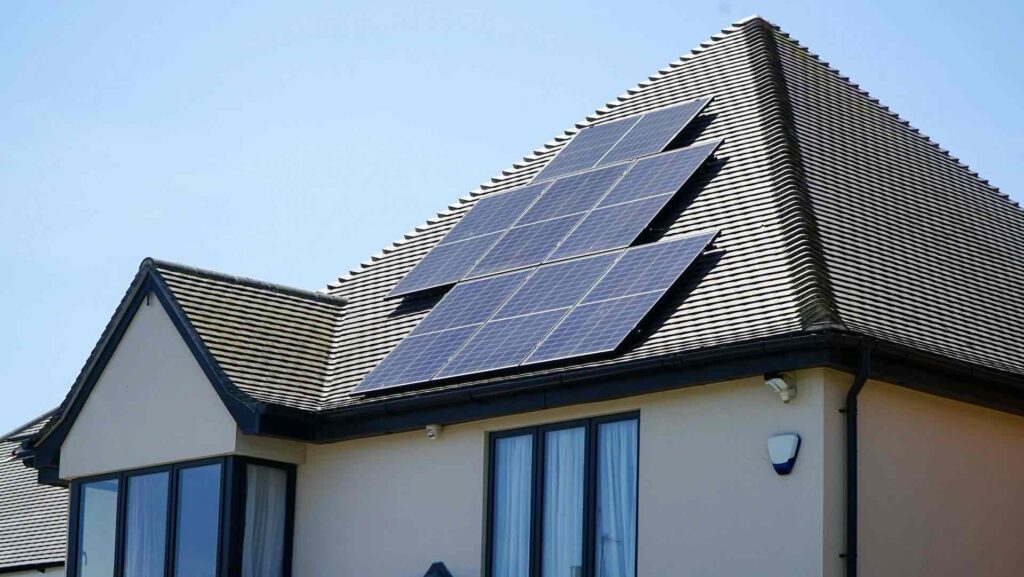 Ein modernes Haus mit zahlreichen Solarmodulen auf einem Schrägdach unter strahlend blauem Himmel, das verdeutlicht, wie erneuerbarer Strom herkömmliche Heizsysteme wie die Nachtspeicherheizung in energieeffizientere Lösungen verwandeln kann.
