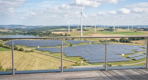 Der Blick vom Balkon auf Felder mit Solaranlagen und Windkraftanlagen inmitten einer ländlichen Landschaft unter einem teilweise bewölkten Himmel – eine inspirierende Szene, die den Geist der Energiewende 2026 einfängt.