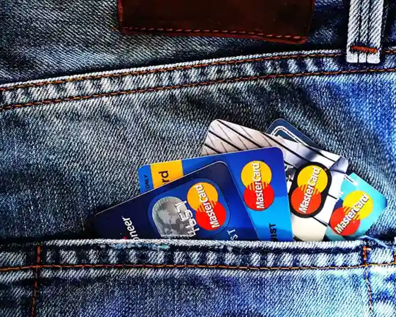 Mehrere Kredit- und Debitkarten, darunter MasterCard, ragen teilweise sichtbar aus der Vordertasche der Blue Denim-Jeans heraus, ähnlich wie beim Vergleich des täglichen Zugriffs auf Tagesgeld- und Festgeldkonten.