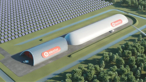 Luftaufnahme von zwei großen, weißen Industriegebäuden mit der Aufschrift „elestor“, umgeben von Solarmodulen und Bäumen, mit einer Straße und zwei geparkten Autos neben den Gebäuden – hier wird modernste Wasserstoff-Eisen-Batterie-Technologie entwickelt.