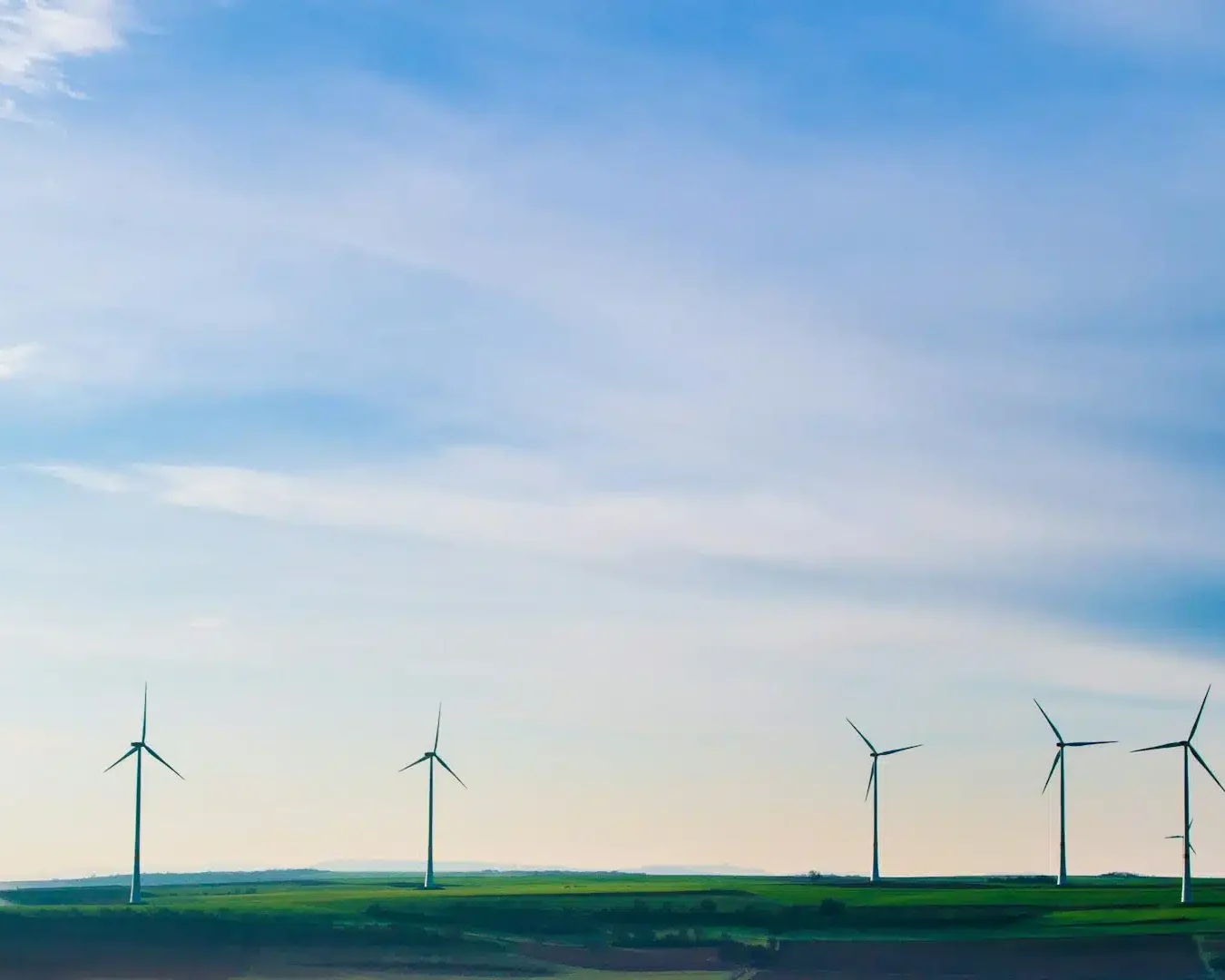 Windturbinen stehen in einer Reihe in einer grünen Landschaft unter einem strahlend blauen Himmel mit leichten Wolken und fangen erneuerbare Energie für eine nachhaltige Zukunft ein - eine inspirierende Szene, die oft in ESG-Reporting beleuchtet wird.