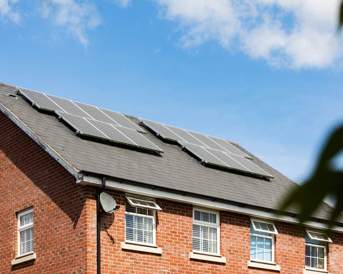 Ein Backsteinhaus mit drei Solarpaneelen auf dem dunkelgrauen Dach unter einem teilweise bewölkten blauen Himmel.
