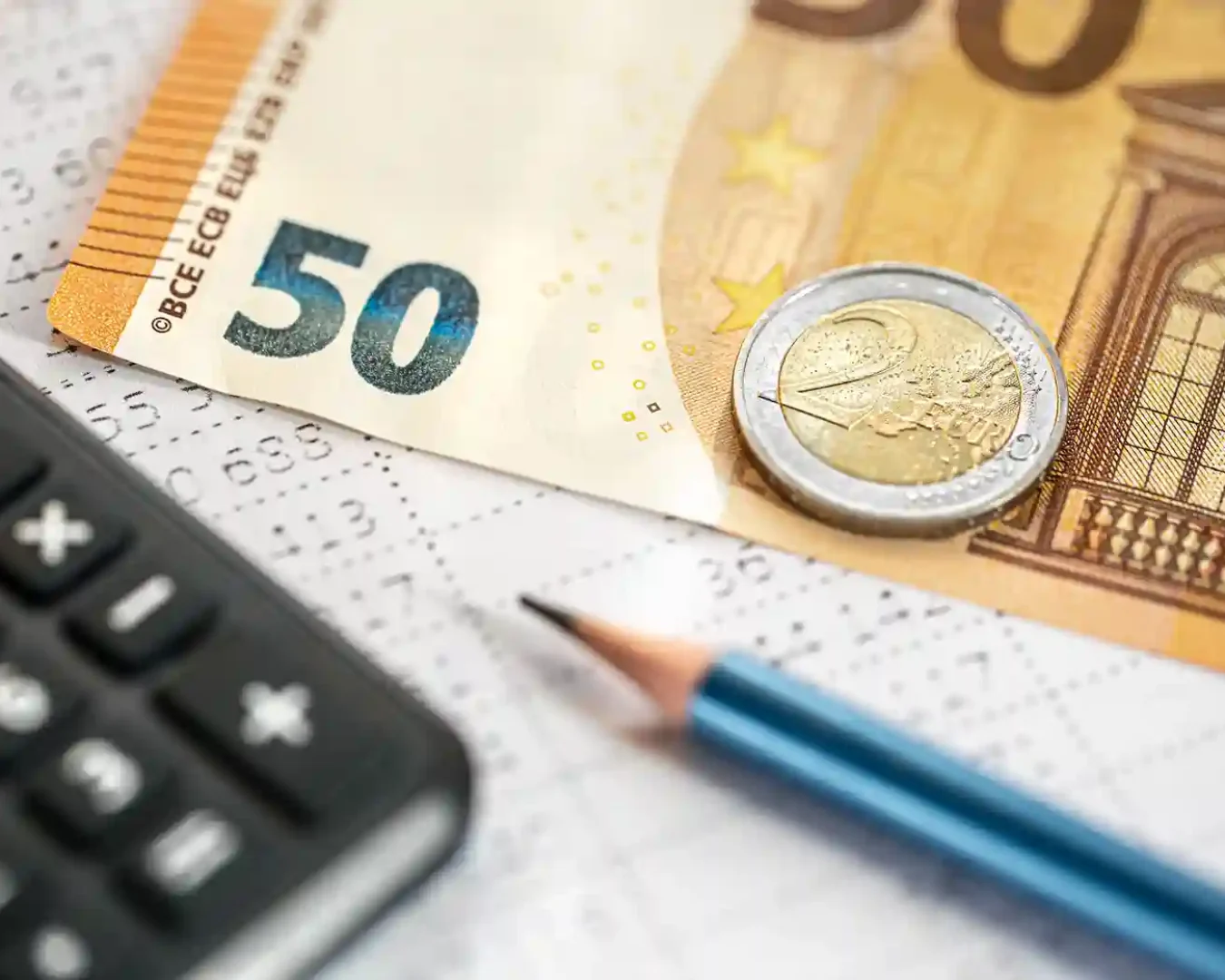 Eine Nahaufnahme einer 50-Euro-Banknote, einer 2-Euro-Münze, eines Bleistifts und eines Taschenrechners - ideale Werkzeuge für die Verwendung eines Zinsrechner-Festgelds -, die auf Finanzdokumenten mit aufgedruckten Zahlen liegen.