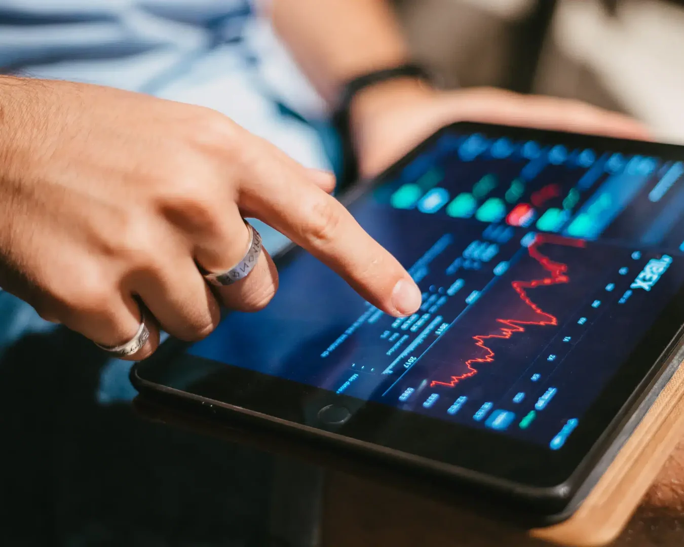Eine Person berührt mit einem Finger ein Tablet, auf dem Börsencharts und Finanzdaten mit roten und grünen Graphen angezeigt werden, und recherchiert möglicherweise Themen wie "wie funktioniert ein ETF"